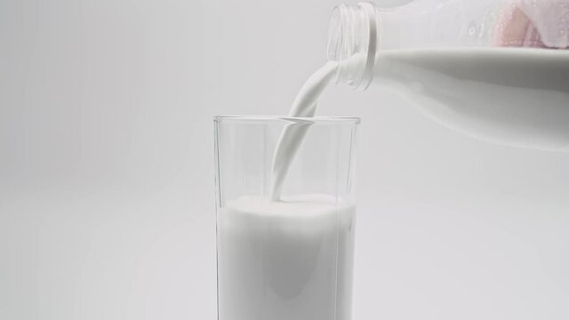 Daily dose of milk. Shot of pouring, splashing fresh milk into a transparent glass against white background. Dairy product concept. Filling glass with milk close up. 4K video
