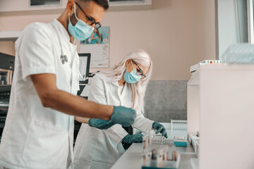 Two hardworking medial workers holding test tubes with blood samples and working on cure for...