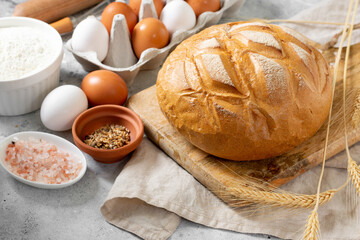 Wheat round bread. Wheat bread is surrounded by baking ingredients. Bread close-up. Eggs, salt, flour, seeds on the kitchen table