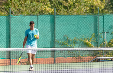 Obraz premium Professional tennis player on tennis court selects the ball for serve. Playing tennis on open hard courts. Sports background. Selective focus.