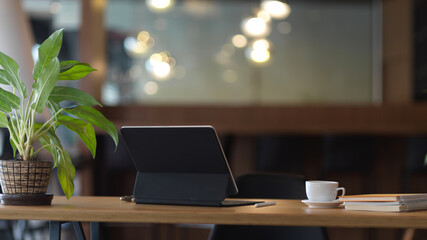 Worktable with digital tablet, coffee cup, notebooks and plant pot in office room