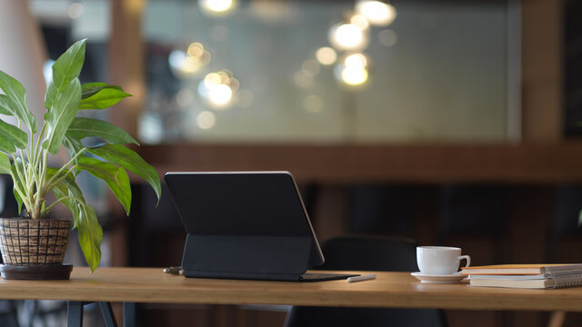 Worktable with digital tablet, coffee cup, notebooks and plant pot in office room