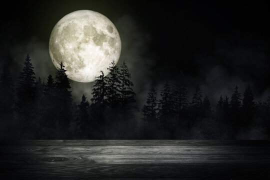 Wooden table top with forest in the dark night and fog or mist with full moon in background. (Elements of this image furnished by NASA.)