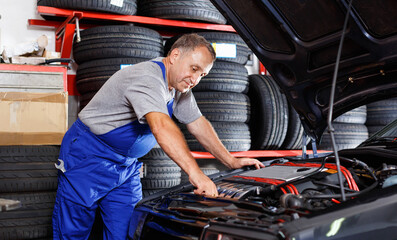 Professional mature glad cheerful positive smiling man car mechanician repairing car in auto repair shop
