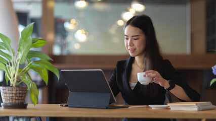 Businesswoman holding coffee cup while working with office supplies