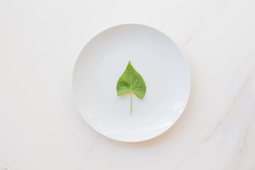The concept of diet and weight loss, fasting and cleansing the body. Empty white plate on a white marble table. Detox the body with green foods