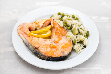 fried salmon with rice with vegetables on white plate on ceramic background