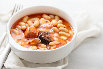 typical spanish dish fabada, beands with smoked sausages and meat on white dish