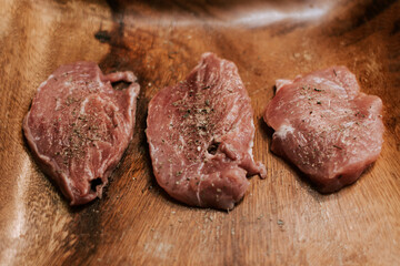 Raw three beef and pork steaks on a cutting board with spices