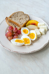 Homemade Healthy Organic Breakfast Plate with Boiled Eggs, Cheese, Fruits and Sourdough Bread Slices.