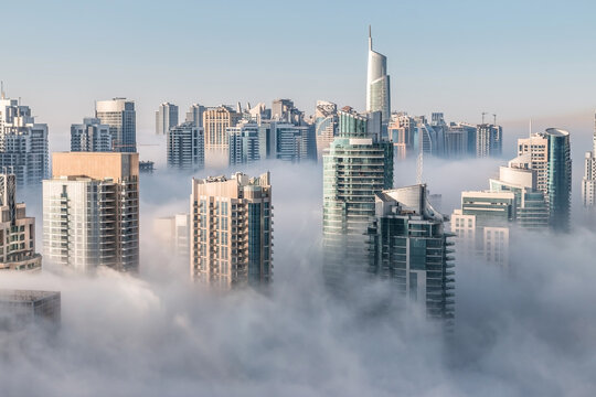 Morning fog hovering skyscrapers at sunrise. Building rooftops over the clouds in Dubai Marina