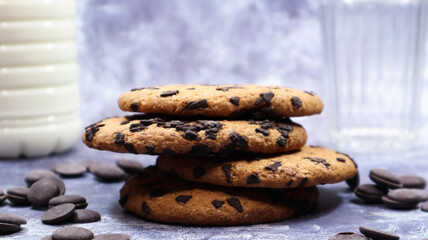 American chocolate chip cookies stacked on top of each other with milk in a glass on a gray background. Traditional rounded crunchy dough with chocolate chips. Bakery. Delicious dessert, pastries.