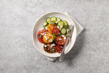 salad of fresh farm tomatoes, basil, feta cheese and olive oil on a light concrete background
