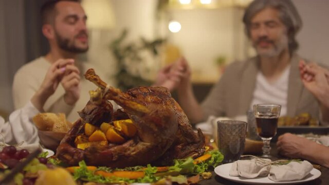 Roasted turkey focused shot footage of four Caucasian people sitting together at dinner table praying to God on Thanksgiving day