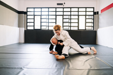 Three partners in a martial arts training such as judo or karate with kimonos practicing techniques on the gym mat all wearing face masks due to the covid 19 coronavirus pandemic