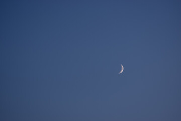 Clean background with the sky and moon on the desktop and a lot of empty space for text. The Crescent moon lit up in the blue night sky with a bright yellow glow. Moon in the sky, horizontal banner.