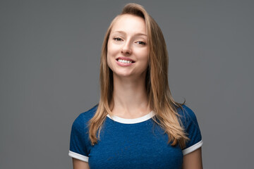 Image of young happy woman smiling and looking at camera, wearing in casual blue t shirt. Studio shot, gray background