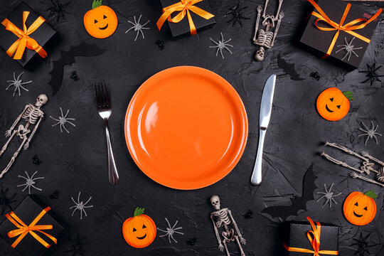 Halloween table setting with cutlery, spooky decorations and gifts on black table.