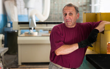Fototapeta premium Portrait of elderly foreman in protective gloves standing in workshop. High quality photo