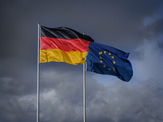 EU and Germany waving flags with grey cloudy dramatic sky on background
