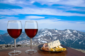 Two glasses of red wine with snacks assortment against mountain background. View of snowy peaks in the mountains.