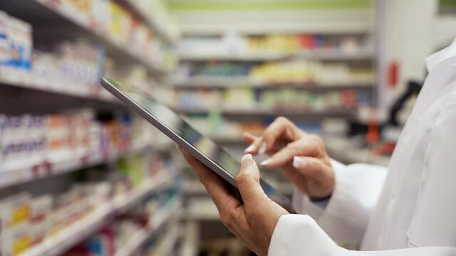 Close up of female pharmacist scrolling through prescriptions on digital tablet standing in white coat in clean pharmacy 