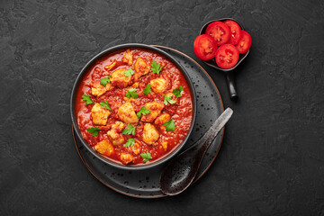 Chicken Madras Curry in black bowl on dark slate table top. Indian cuisine dish with with chicken meat and spicy masala gravy. Asian food and meal. Top view