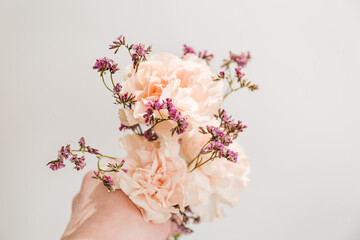 bouquet of flowers in the hand on the tint blue background, symbol of love, pink or beije carnations and small branch