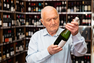Attentive elderly man chooses champagne in a liquor store. High quality photo