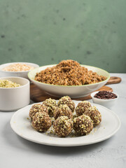 Home made vegan energy protein balls with oats, nuts, dates, dried fruit, flax and hemp seeds, chocolate nibs and maple syrup on white dish over gray and green stone background.