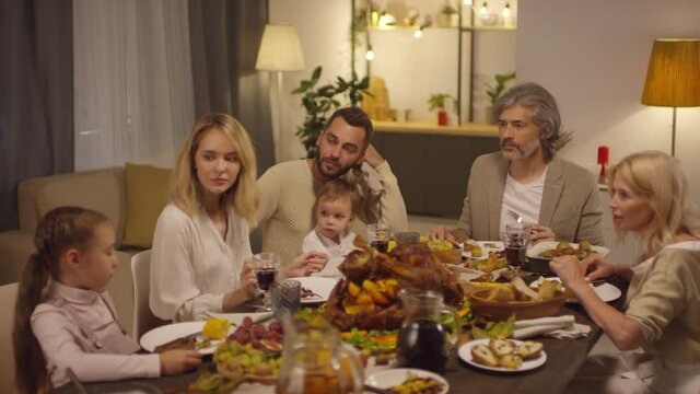 Multi-generation family members sitting together at table talking about something while celebrating Thanksgiving holiday
