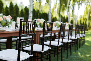 chairs and dinner tables with white cloth, served with porcelain and green glasses. Georgeous wedding table decorated with flowers on a green lawn