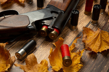 Hunting rifle and cartridges on a wooden background with yellow leaves.