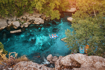 Aerial view of water tourists in a boat during an extreme rafting by a blue mountain river in deep canyon and gorge - obrazy, fototapety, plakaty