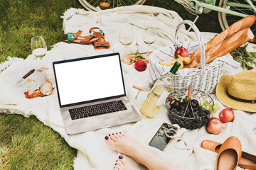 Laptop computer and french style outdoor picnic - wicker basket and food