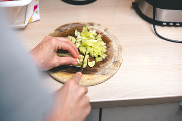 Woman's hands cutting fresh paprika on chopping board, over the shoulder view. Cooking at home concept.