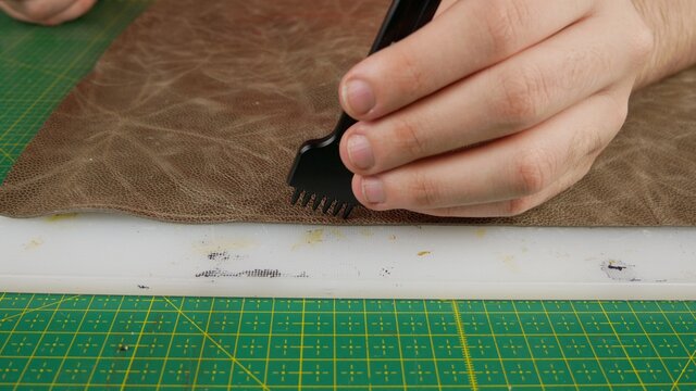 a professional punches holes in the skin with a round punch on a white board against the background of a self-healing green mat