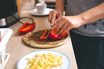 Woman's hands cutting fresh red paprika on chopping board.  Cooking at home concept.