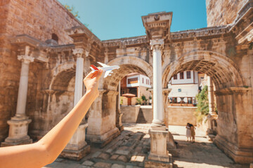 traveler with a toy plane on the background of the archaeological monument - the gate of the Emperor Hadrian in the old city of Antalya. Concept of air tickets and airlines in Turkey