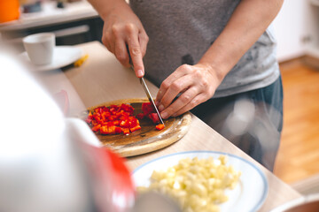 Woman's hands cutting fresh red paprika on chopping board.  Cooking at home concept.
