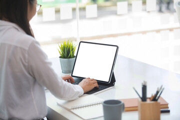 Cropped shot of Business women are using a tablet showing a white screen to put your text and pictures  working on a table beside the window.