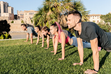 Group of young people practicing plank exercise in fitness session, in the park in the city of Palma de Mallorca