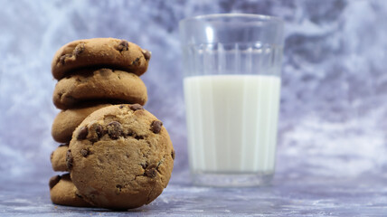 American chocolate chip cookies stacked on top of each other with milk in a glass on a gray background. Traditional rounded crunchy dough with chocolate chips. Bakery. Delicious dessert, pastries.