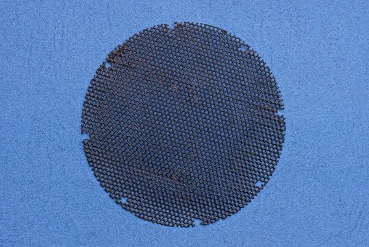 one round old black iron mesh for the fan hood lies on a blue table