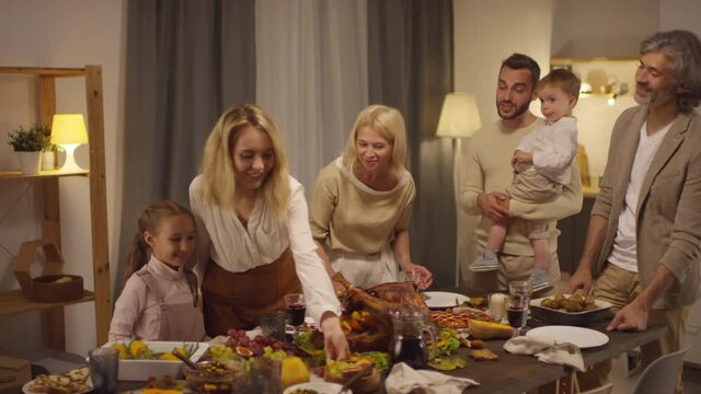 Happy big family with kids spending Thanksgiving evening together gathering at dining table, medium long shot footage