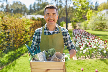 gardening and people concept - happy smiling middle-aged man in apron with tools in box at summer garden