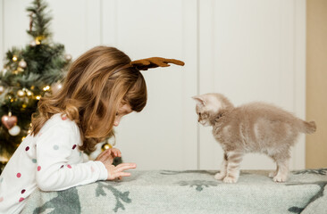 Funny small girl with  little kitten.Christmas tree background.