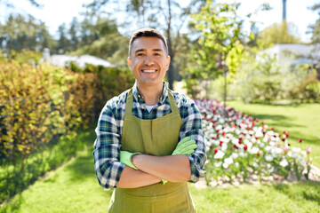 gardening and people concept - happy smiling middle-aged man in apron with crossed hands at summer garden