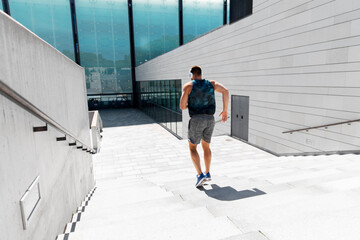 fitness, sport, training and lifestyle concept - young man in headphones running downstairs outdoors