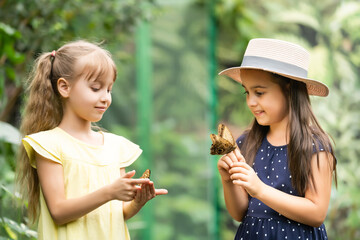 two little girls with butterflies in a greenhouse